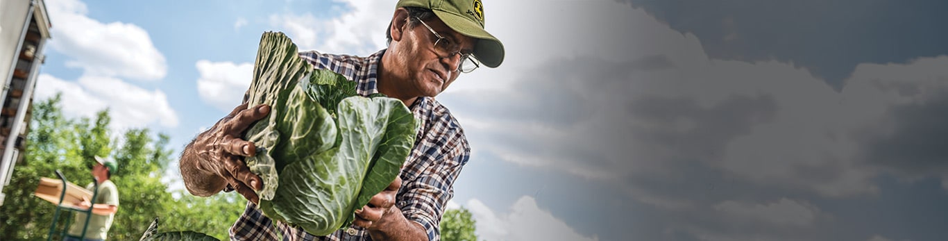 Vyras su sunkia kepure darbo vietoje su John Deere įranga netoliese