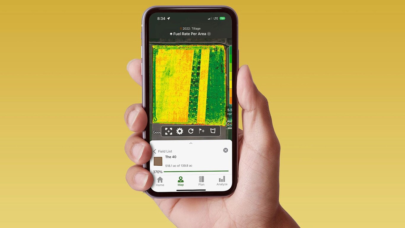 Ranka laikydami išmanųjį telefoną, kuriame rodomas John Deere Operations Center su degalų sąnaudų duomenimis.
