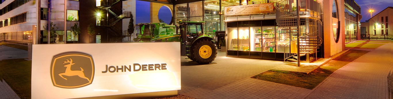 „John Deere“ būstinės pastato su tvenkiniu ir gluosniais priekiniame plane vaizdas iš priekio