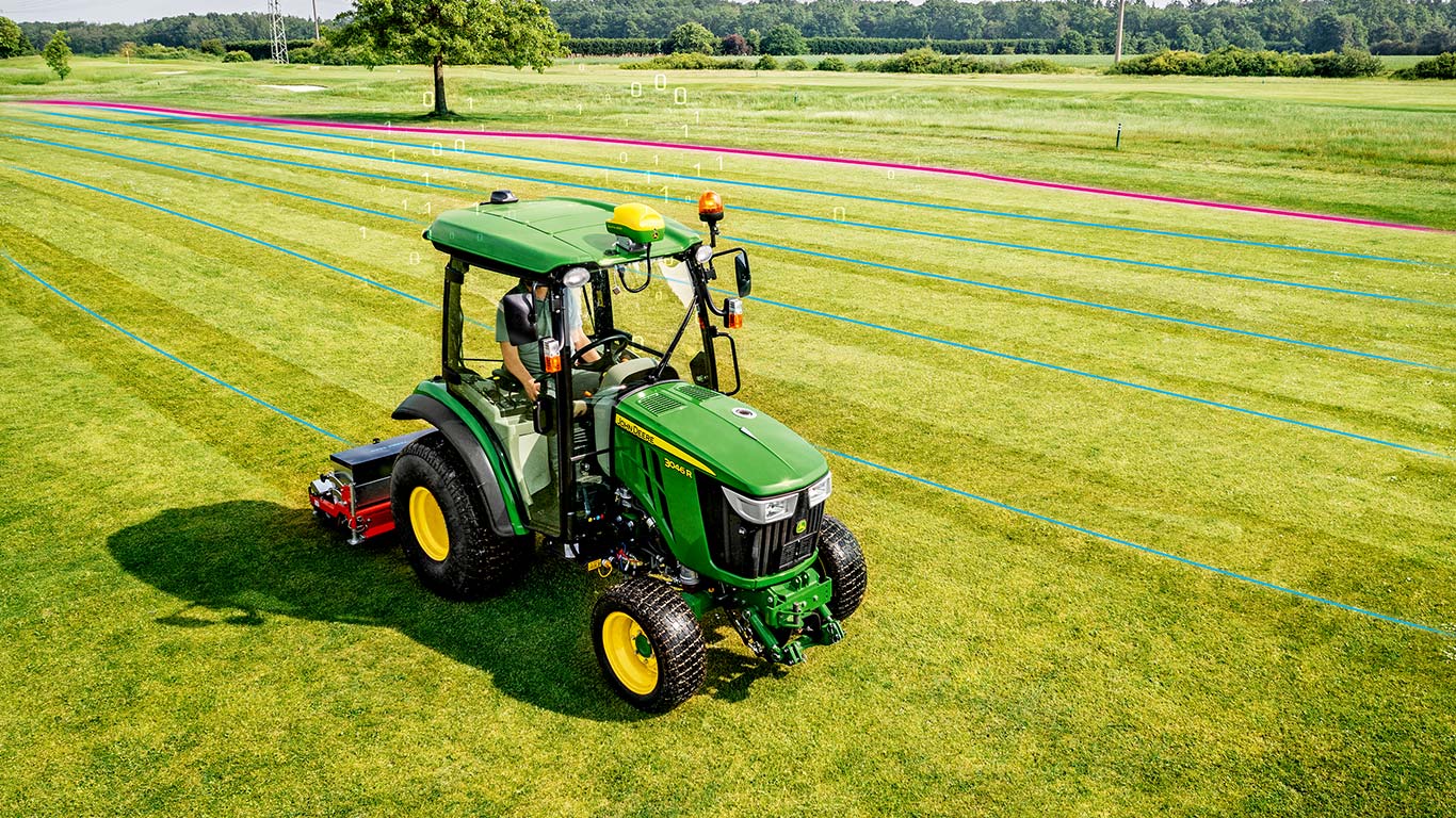 Vejos priežiūrėtojas dirba vejos plote su John Deere kompaktišku universaliuoju traktoriumi.