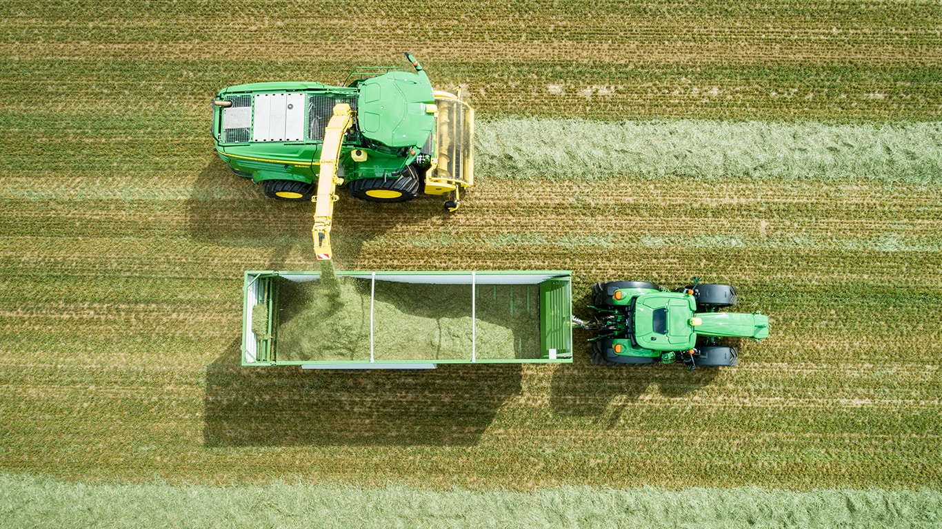 Vaizdas i&scaron; &bdquo;John Deere 8000&ldquo; serijos savaeigio pa&scaron;arų kombaino galo su dviem silosiniais vežimais, kuriuos &bdquo;John Deere&ldquo; traktoriai traukia tiesiai i&scaron; paskos