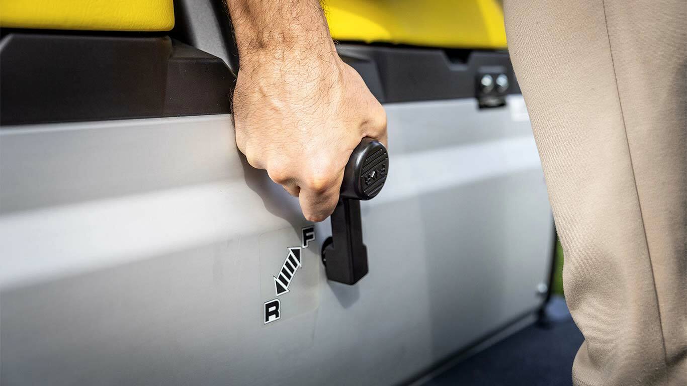 "John Deere Gator GS" rankinio pavarų perjungimo svirties valdymo, rodančio priekinės ir atbulinės eigos padėtis šalia geltonų sėdynių, vaizdas iš arti.