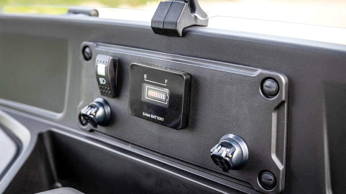 "John Deere Gator GS" elektrinio modelio prietaisų skydelis, kuriame rodomas akumuliatoriaus lygio indikatorius ir maitinimo prievadai.