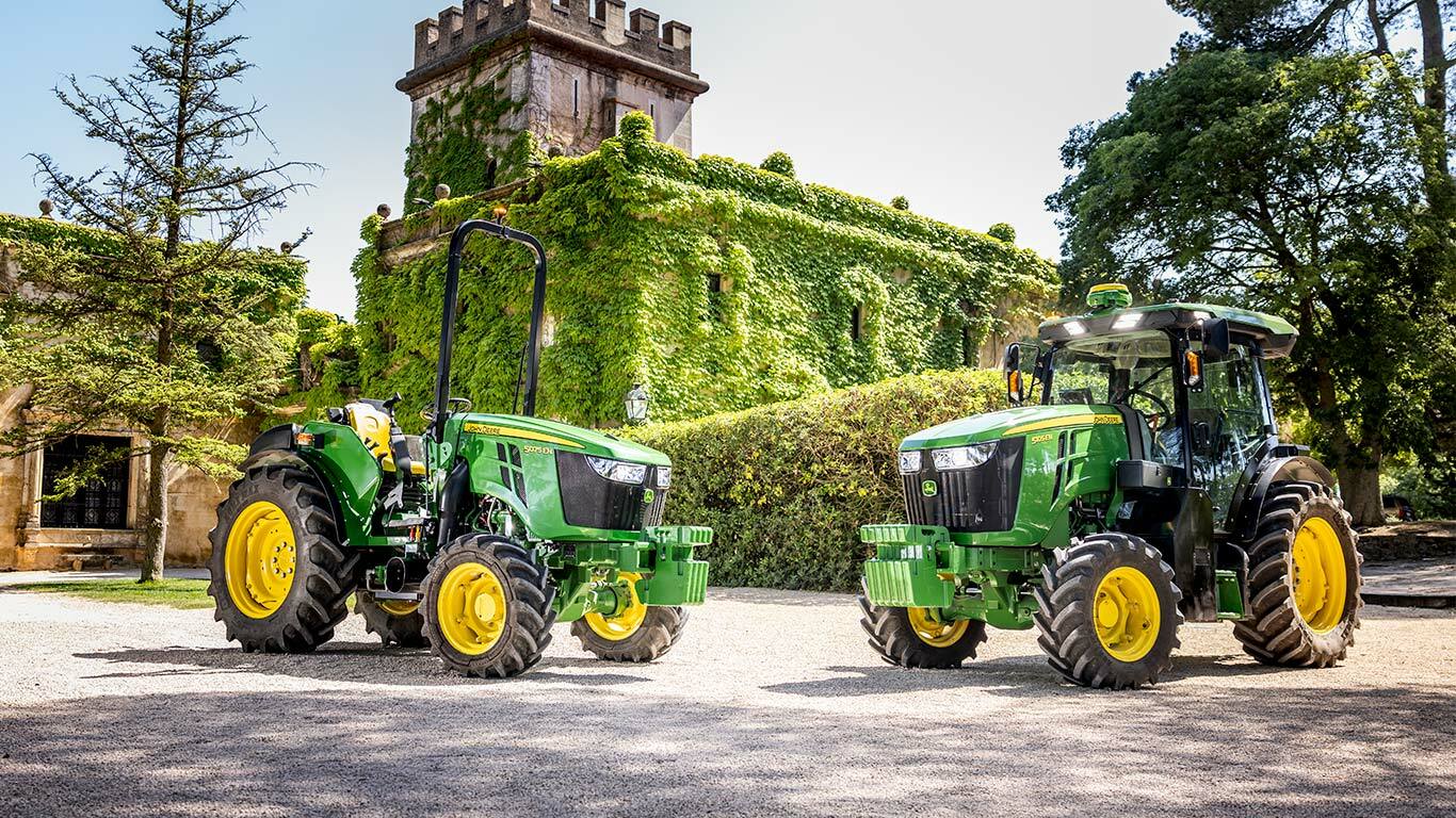 Žalio ir geltono „John Deere“ traktoriaus 5015EN vaizdas iš viršaus: traktorius velka purkštuvą tolygiai išdėstytomis vaismedžių eilėmis