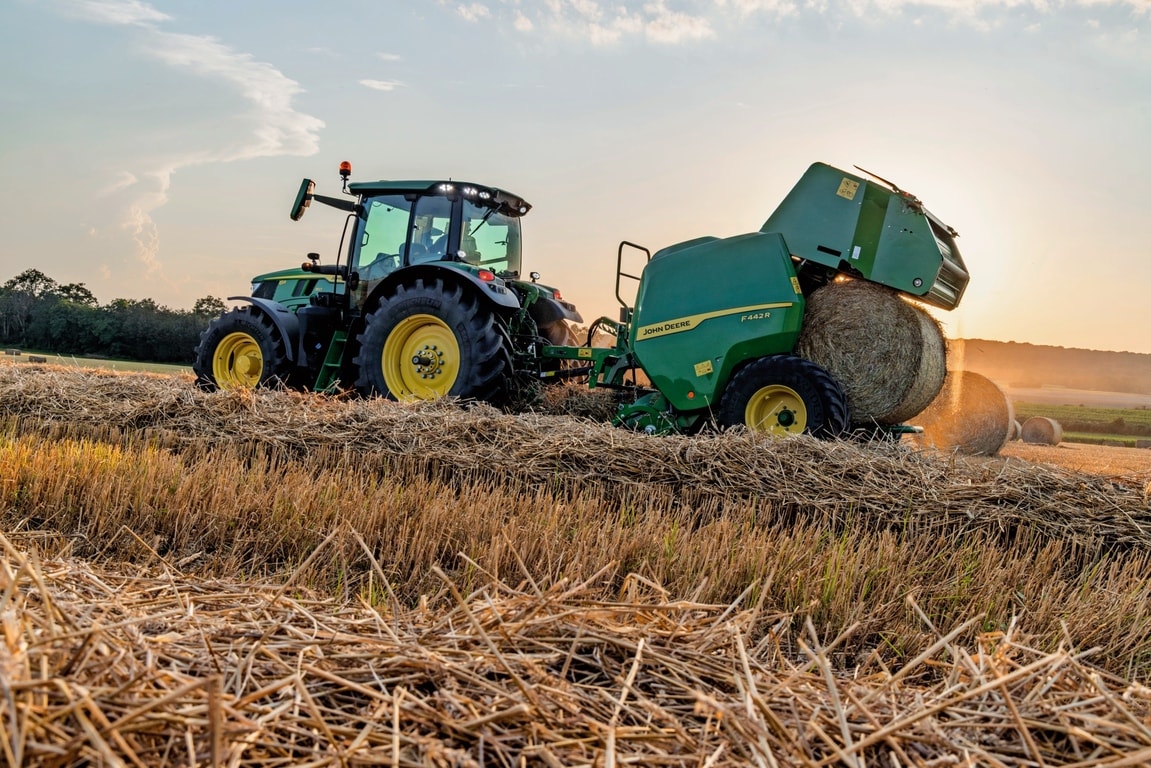 John Deere 6M traktoriaus velkamas F442M ryšulių presas, išmetantis šiaudų ryšulį